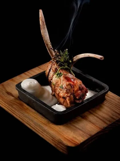 Smoked lamb chop, presented with a wisp of smoke, highlighting the care and technique that goes into our grilled dishes.