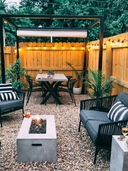 This modern setup features a fire pit and sleek, dark-toned furniture under a simple pergola frame. The gravel ground cover is a practical and stylish choice for a low-maintenance entertainment space.