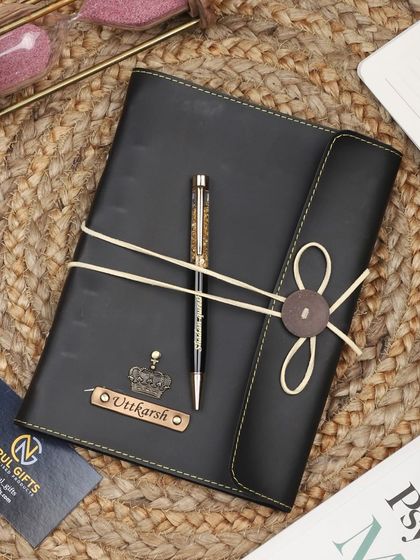 A black leather thread-bound diary and pen set with a crown charm.