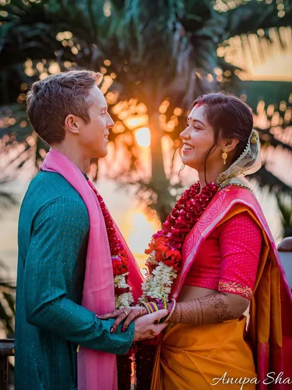 A beautiful sunset portrait of a couple on their wedding day. The warm, golden light of the setting sun creates a romantic backdrop, highlighting their traditional garments and happy expressions.