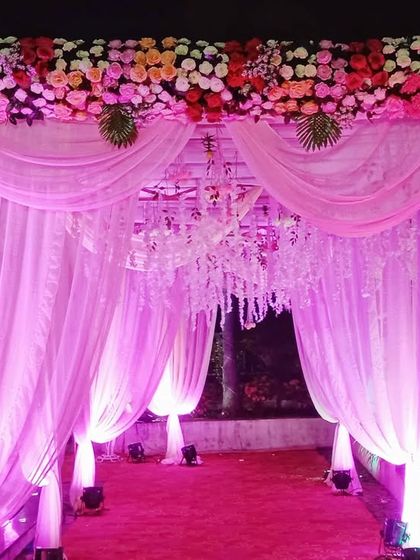 A beautiful floral entrance gate for an evening event, with pink drapes, a crystal chandelier, and dramatic pink uplighting.