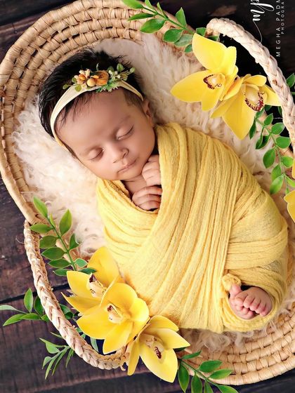 A close-up from the side, highlighting the baby's peaceful expression and the fresh green leaves mixed with the flowers.