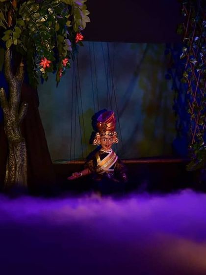 The use of colored lighting, here a deep purple, helps to set the mood for different scenes. Two puppets are seen in a quiet, intimate moment amidst the dramatic fog.