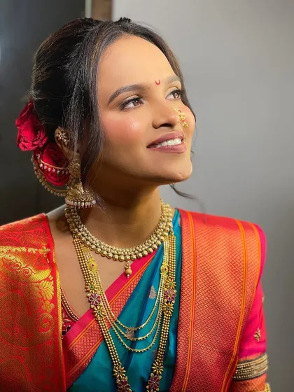A side profile showing the intricate hairstyle adorned with a red rose. The glowing skin and defined eyes are hallmarks of my signature bridal style.