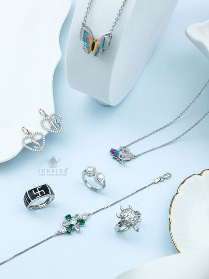 A statement in silver. This image displays a range of my custom silver pieces, including a butterfly pendant, initial heart charms, a men's Swastik ring, and a delicate bracelet with green gemstones.