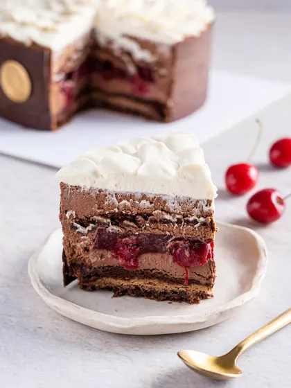 A perfect slice of our modern Black Forest Entremet, revealing layers of rich chocolate mousse, tangy cherry confit, and light whipped cream. This is a sophisticated reinterpretation of a classic, showcasing our dedication to flavour and texture.