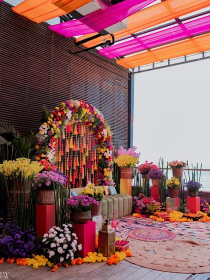 The stunning and colorful decor setup for a Mehendi carnival, featuring a floral arch and vibrant seating.
