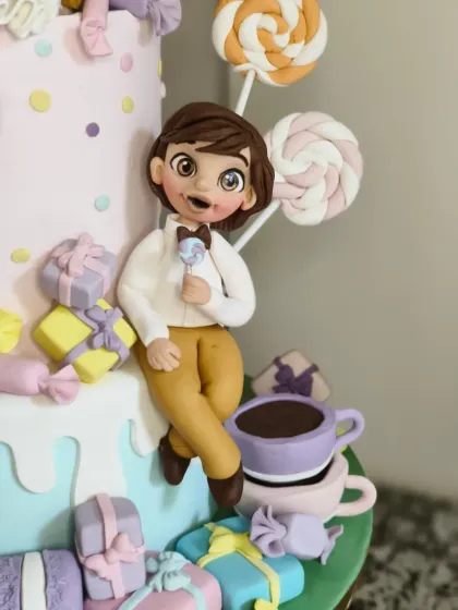 The equally detailed boy figurine from the Candyland cake, enjoying a lollipop. His cheerful expression and dapper little outfit add to the whimsical charm of the whole piece.