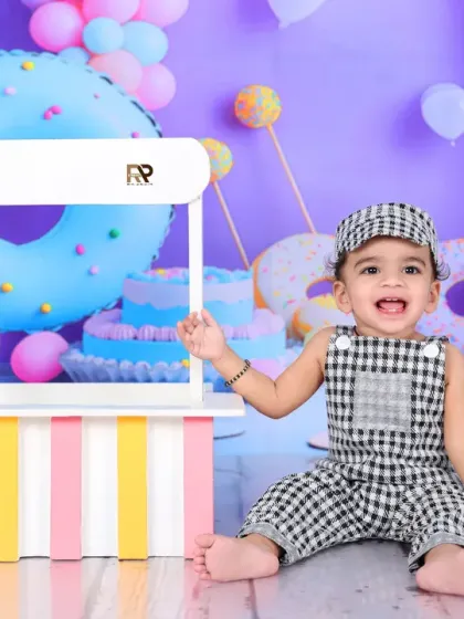 A happy baby boy enjoys his time in the candy-colored sweet shop. The checkered outfit and joyful expression make this a truly delightful photo.