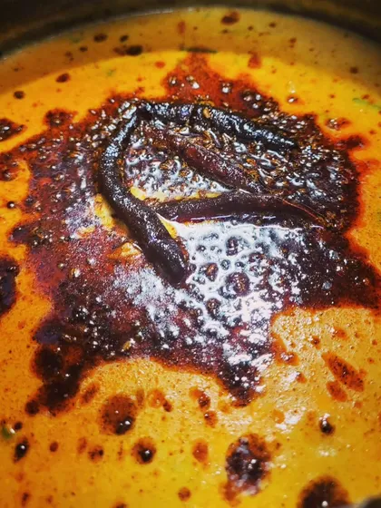 The rich red color of the chili in the tadka contrasts beautifully with the yellow kadhi.