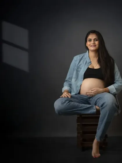 A confident and modern solo maternity portrait. The relaxed, cross-legged pose on a simple wooden crate exudes a cool, effortless style.