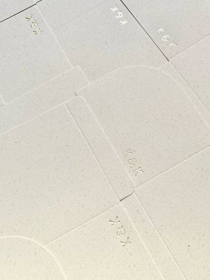 A sheet of textured, handmade paper with the 'K&K' monogram subtly debossed. The texture of the paper itself adds a layer of understated luxury.