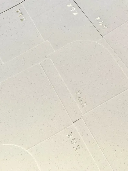 A sheet of textured, handmade paper with the 'K&K' monogram subtly debossed. The texture of the paper itself adds a layer of understated luxury.
