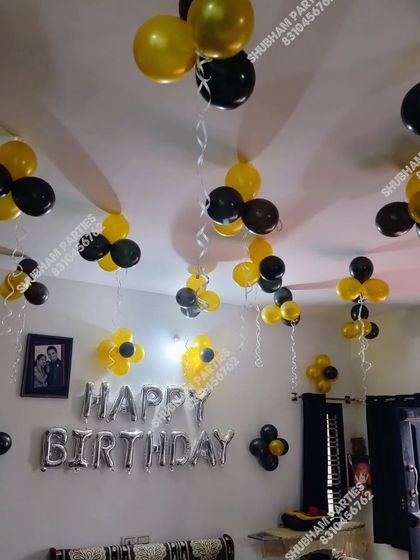 A simple birthday setup with black and yellow balloon bunches and "Happy Birthday" foil letters.