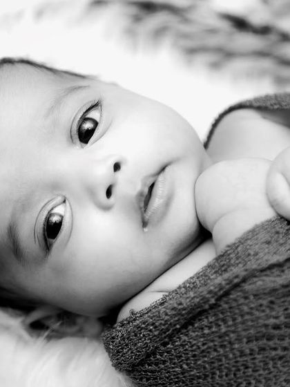 A striking black and white portrait of an awake twin. The monochrome tones highlight their beautiful eyes and curious expression.