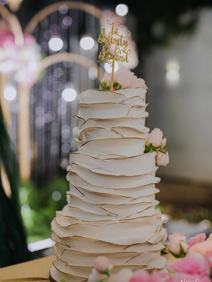 A close-up of a beautiful tiered wedding cake with a "To Infinity and Beyond" topper. We coordinate with the best bakers to ensure every detail, including the cake, is perfect.