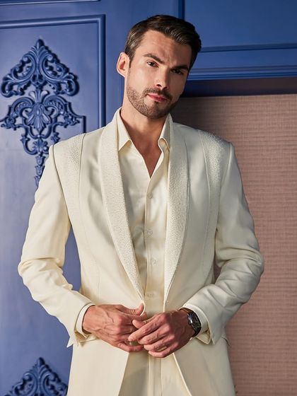 This front-on view of the ivory tuxedo emphasizes the clean lines of the shawl collar and the meticulous beadwork. The bespoke fit ensures a powerful and flattering silhouette.