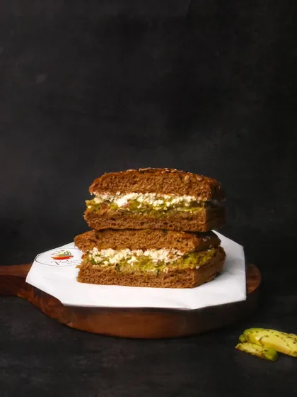 A healthy sandwich with a green, herby filling, presented on a dark wooden board. The dark background contrasts with the light paper, drawing the eye to the sandwich.