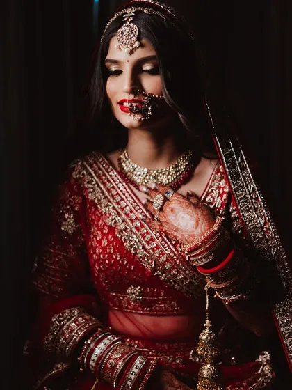 A dramatic, low-light portrait of a bride in red. The bold red lip and defined eyes create a look of intense beauty and timeless elegance.