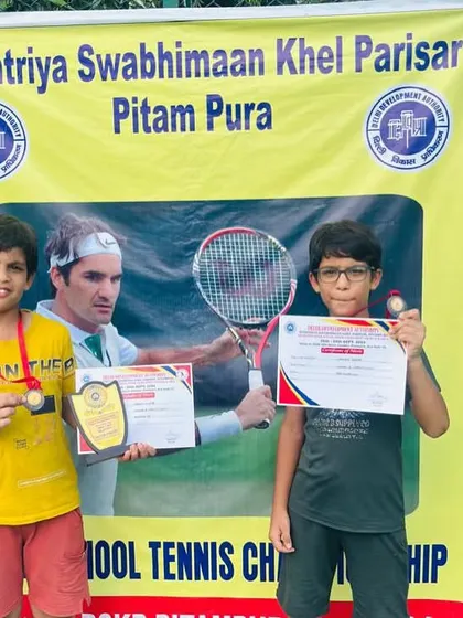 Two of my young champions, Garvit and a fellow player, posing with their trophies and certificates in front of the tournament banner. Their smiles show the joy of achievement.