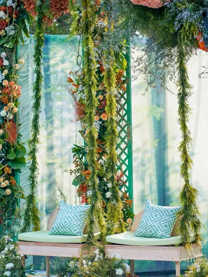 A whimsical swing set for a Mehendi, draped in lush moss and florals, with a serene forest-printed backdrop creating a perfect, dreamy photo opportunity.