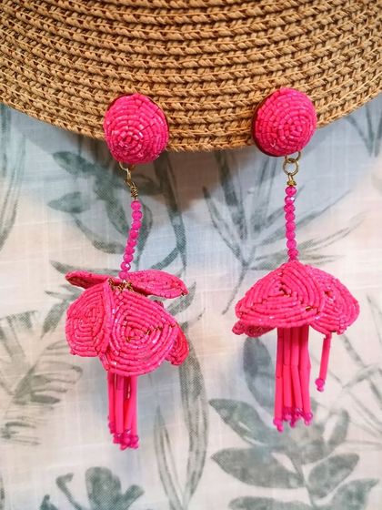 A styled shot of the fuchsia floral beaded drop earrings against a straw hat and leafy background.