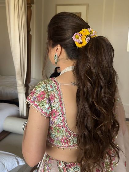 Soft beachy curls in a high ponytail, adorned with fresh yellow flowers. This is a fresh and youthful hairstyle, perfect for a sunny morning Haldi ceremony.