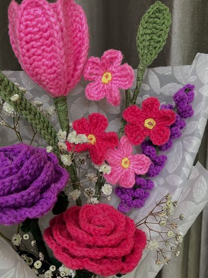 A closer look at the vibrant colors in this handmade bouquet. You can see the detailed stitch work in the purple rose, the pink tulip, and the smaller filler flowers, all crafted from yarn.