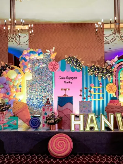 A sweet and colorful Candyland and ice cream parlor theme. This vibrant setup includes giant lollipop and ice cream cone props, a shimmering backdrop, and custom-themed cake stands.