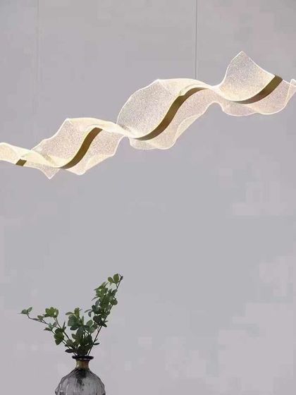 A simple and elegant ribbon-like pendant light, shown here in a minimalist setting. Its gentle curve adds a soft, artistic touch.