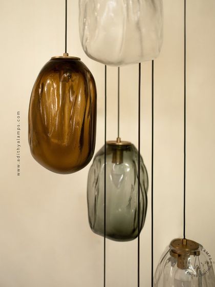 This cascading installation features pendants made of organic, free-form glass in smoked and amber tones. The textured, irregular shapes create a beautiful, water-like effect, perfect for adding a sense of calm and artistry to a room.