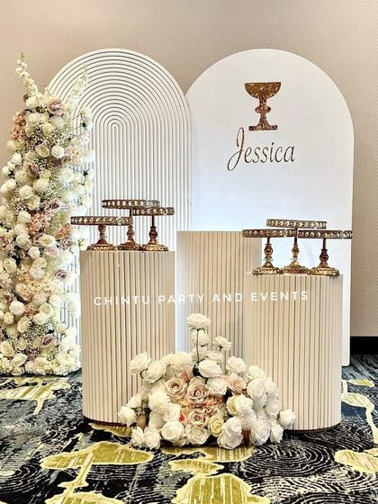 An elegant christening decoration for a baby girl. This sophisticated setup uses white ridged pedestals and backdrops with delicate floral arrangements.