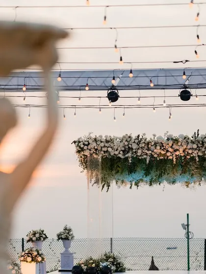 A closer look at the floating floral arrangement above the sundowner mandap. The dense canopy of white flowers and greenery appears to hang in mid-air against the evening sky, adding to the magical feel.