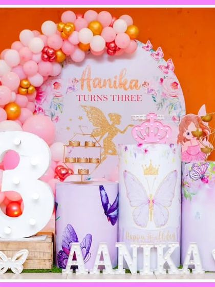A beautiful butterfly and fairy-themed third birthday. The pink and gold decor features a 'Aanika' marquee, a large light-up number '3', and whimsical cutouts.