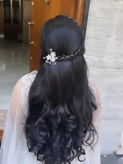 A beautiful half-up hairstyle with a braided crown and soft curls, perfect for a sangeeth or reception.