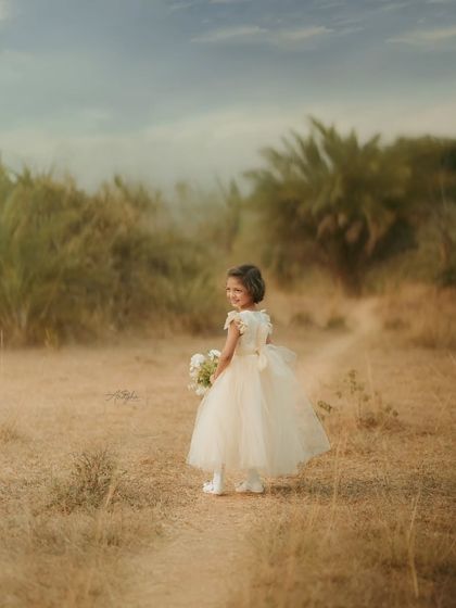 A girl in a formal dress looks back over her shoulder while walking down a path in a rustic, grassy field.