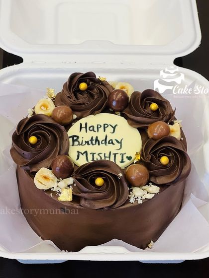 A rich chocolate bento cake for Mishti's birthday. It's decorated with chocolate rosettes, crunchy hazelnuts, and gold leaf for an elegant touch, perfect for an intimate celebration.