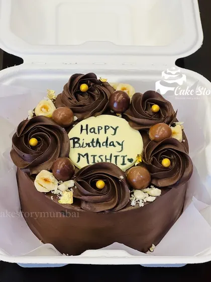 A rich chocolate bento cake for Mishti's birthday. It's decorated with chocolate rosettes, crunchy hazelnuts, and gold leaf for an elegant touch, perfect for an intimate celebration.