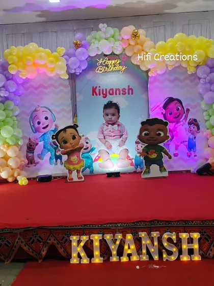 A fun and colorful Cocomelon theme, perfect for a first birthday party. This stage decoration includes a pastel balloon arch, character cutouts of JJ and his friends, and a large light-up number one.
