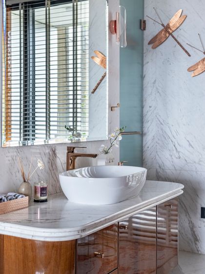 A modern washroom in the Filigree House, featuring a vanity with beautiful dragonfly-shaped metal art. The design combines glossy wood finishes with white marble for a sophisticated and artistic touch.