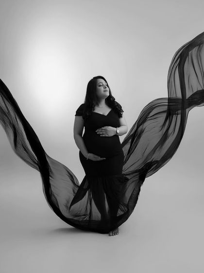 A classic black and white portrait. The flowing fabric creates a beautiful, wing-like silhouette, highlighting the mother's form with artistic and timeless elegance.