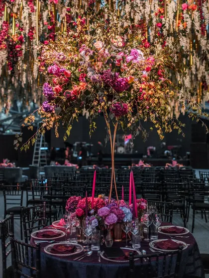 A magnificent floral centerpiece on a guest table, set against a backdrop of hanging wisteria. The scale and artistry of the floral design create a sense of pure opulence.