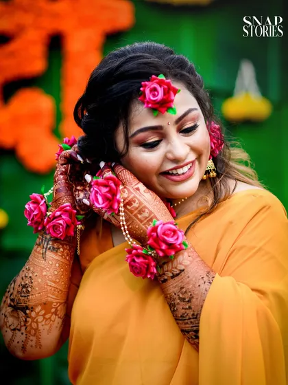 A close-up of the bride, smiling as she adjusts her floral jewelry. We capture the intricate details of your Haldi look, from the floral accessories to the henna.