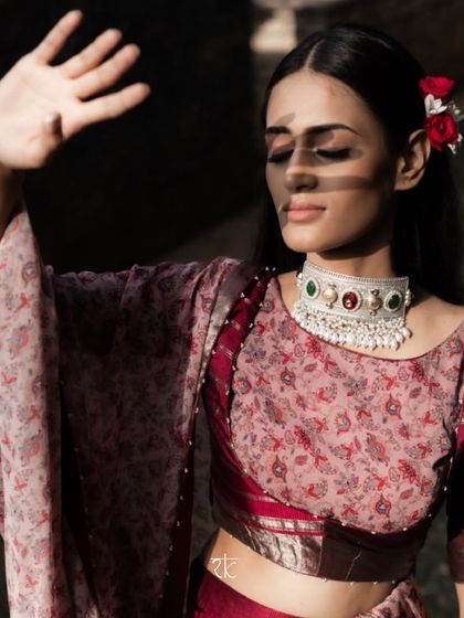 The play of light and shadow highlights the rich maroon color of the silk lehenga and the intricate design of the choker.