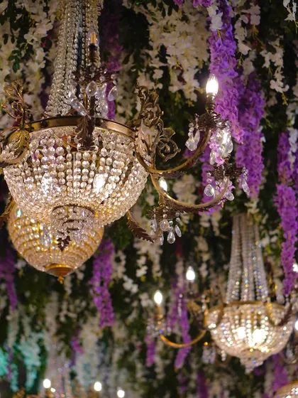 A detail shot of the crystal chandeliers hanging amidst a canopy of purple and white wisteria. This combination of sparkle and soft florals is the essence of modern luxury.