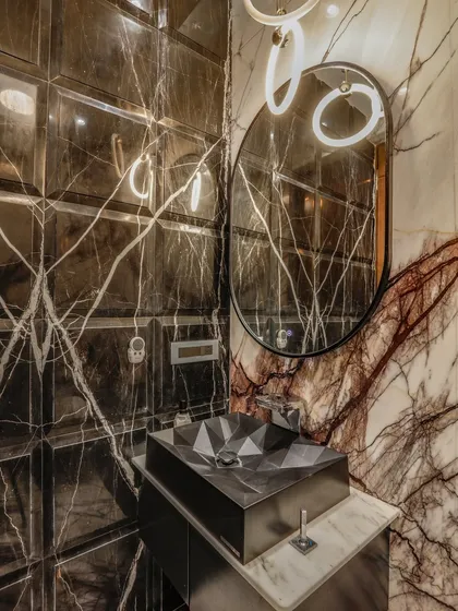 I believe every corner of a home deserves personality. In this powder room, I used bold, dark marble with intricate veining and beveled wall tiles to create a sense of depth. A custom geometric basin and modern ring lighting complete this statement of compact luxury.