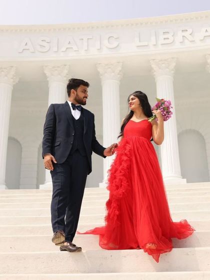 A grand pre-wedding photo at a location that mimics the Asiatic Library. The bright red ruffled gown looks stunning against the white architectural background.