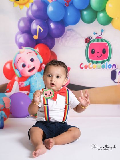 A cute moment where the baby holds up a Cocomelon prop, perfectly matching the theme of his milestone photoshoot.