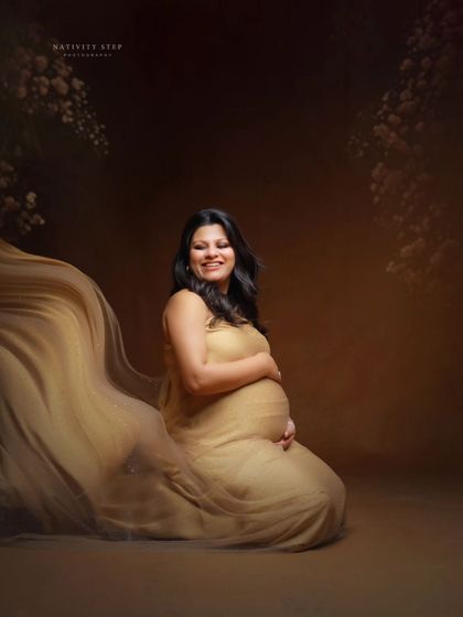 A happy and relaxed seated portrait in a flowing golden gown. The floral elements in the background add a touch of softness and nature.