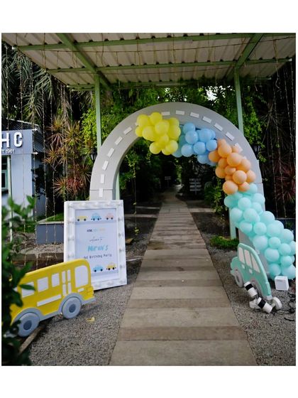 A grand entrance for a vehicle-themed party, featuring a road-style arch, a yellow school bus prop, and a personalized welcome sign.